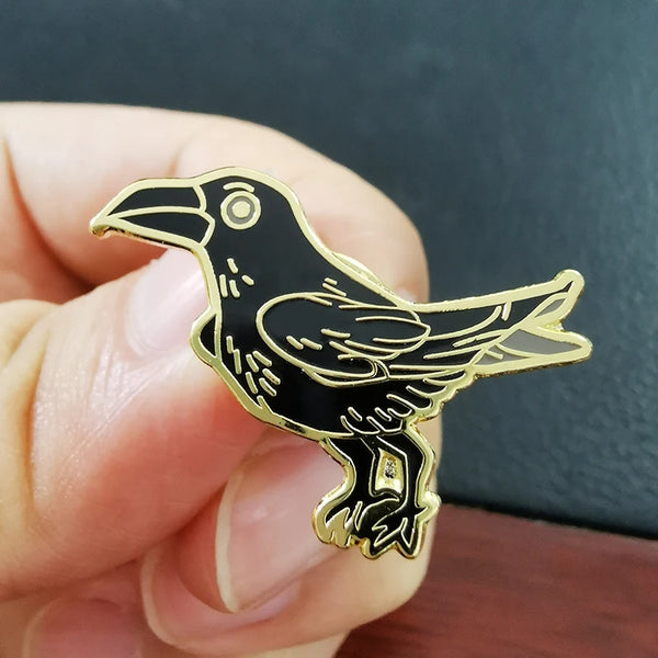 Black raven enamel pin held in hand — front view